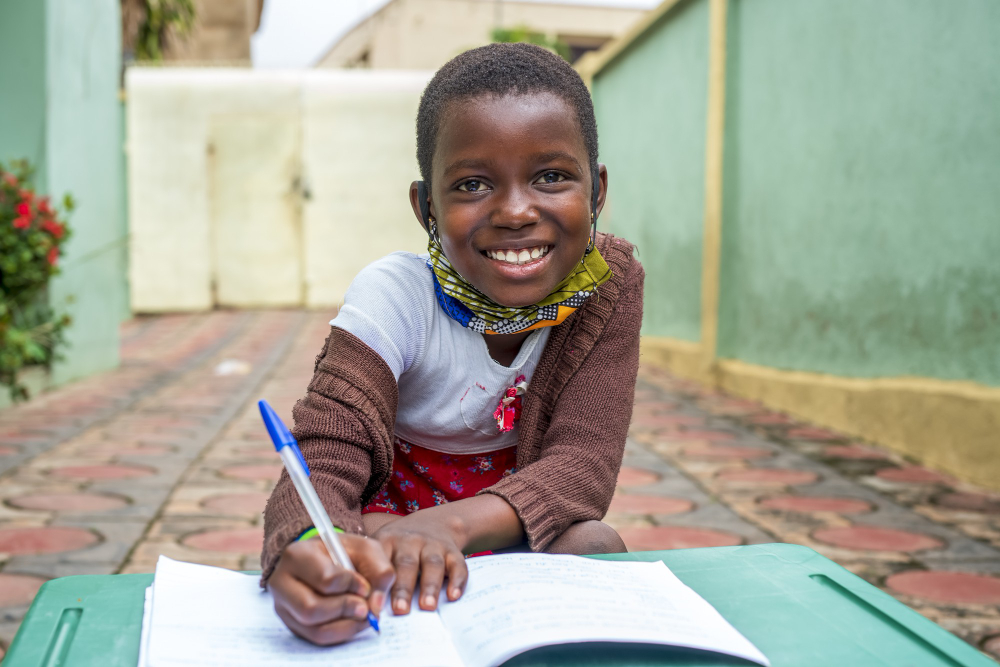 Élève africaine souriante tenant ses livres dans la cour de l'école